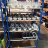 4 SHELVES MIXED LOT CONTAINING VARIOUS LARGE AMOUNT OF GLASSES - COFFEE MUGS - COFFEE MUGS WITH SAUCERS - STAINLESS STEEL JUGS - LARGE AMOUNT OF SPOONS-FORKS AND KNIFES AND FOOD TRAYS ETC